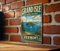 A vintage-style metal sign for Grand Isle State Park in Vermont, featuring a scenic landscape with a sailboat on the water.