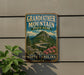 A vintage-style sign for Grandfather Mountain State Park in North Carolina, featuring a scenic mountain landscape with a winding road and pink flowers.