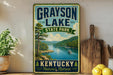 A vintage-style sign for Grayson Lake State Park in Kentucky, featuring a scenic image of a lake surrounded by mountains and trees.