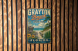 A vintage-style metal sign for Grayton Beach State Park in Florida, featuring a beach scene with palm trees and a path leading to the beach.