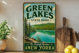 A vintage-style sign for Green Lakes State Park in New York, featuring a scenic image of the lake surrounded by pine trees and mountains.