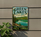 A vintage-style sign for Green Lakes State Park in New York, featuring a scenic image of a lake surrounded by pine trees and mountains.