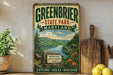 A vintage-style sign for Greenbrier State Park, Maryland, featuring a scenic mountain landscape with a lake and cabin.