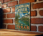 A vintage metal sign for Guadalupe River State Park in Texas, featuring a scenic landscape with a river and mountains.