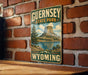 A vintage-style sign for Guernsey State Park in Wyoming, featuring a scenic landscape with a mountain, lake, and trees.