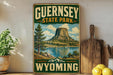 A vintage-style sign for Guernsey State Park in Wyoming, featuring a scenic landscape with a lake, mountains, and a large rock formation.