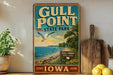 A vintage-style metal sign for Gull Point State Park in Iowa, featuring a seagull flying over a beach landscape with a blue sky and ocean in the background.