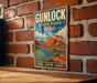 A vintage-style metal sign for Gunlock State Park in Utah, featuring a scenic landscape with mountains, a lake, and desert vegetation.