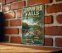 A vintage metal sign for Gunpowder Falls State Park in Maryland, featuring a scenic illustration of the waterfall and surrounding landscape.