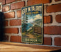 A vintage-style metal sign for Guy W. Talbot State Park in Oregon, featuring a scenic landscape with a path leading to a beach access point.