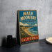 A vintage-style metal sign for Half Moon Bay State Beach in California, featuring a scenic illustration of the bay and coastline.