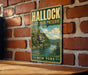 A vintage-style metal sign for Hallock State Park Preserve, featuring a scenic landscape with a river and mountains, mounted on a brick wall.