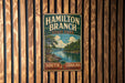 A vintage metal sign for Hamilton Branch State Park in South Carolina, featuring a scenic landscape with a river and pine trees.