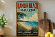 A vintage-style sign for Hamlin Beach State Park in New York, featuring a beach scene with a tree, grass, and water.