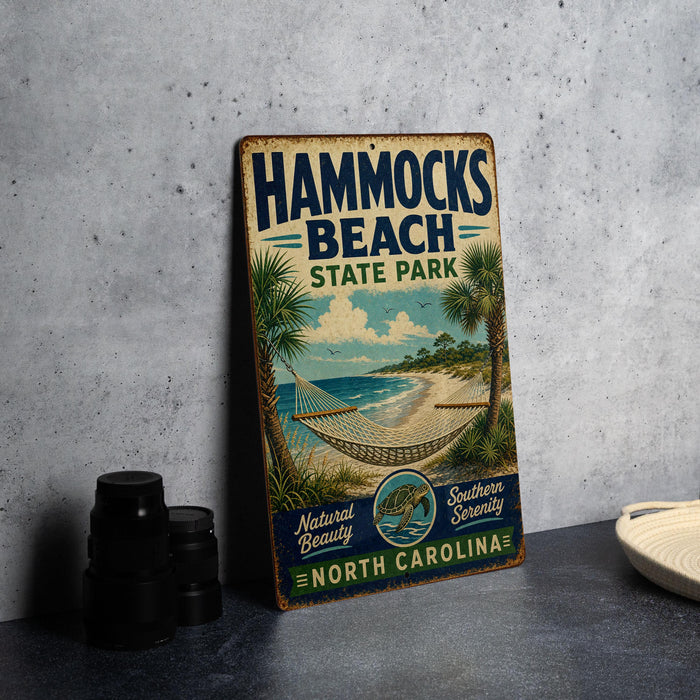 A vintage-style metal sign for Hammocks Beach State Park in North Carolina, featuring a beach scene with palm trees and a hammock.