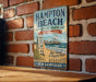 A vintage-style metal sign for Hampton Beach State Park in New Hampshire, featuring a beach scene with a lifeguard tower and a ferris wheel.
