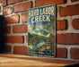 A vintage-style metal sign for Hard Labor Creek State Park in Georgia, featuring a scenic illustration of a lake, mountains, and a cabin.
