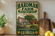 A vintage-style sign for the Hardman Farm Historic Site in Georgia, featuring a farm scene with a barn, house, and tractor.