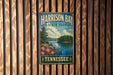 A vintage metal sign for Harrison Bay State Park in Tennessee, featuring a scenic landscape with a lake, mountains, and pine trees.