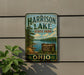 A vintage-style metal sign for Harrison Lake State Park, featuring a scenic lake landscape and the park's name.