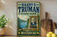 A vintage metal sign for "Harry S. Truman State Park" in Missouri, featuring a portrait of a man and a scenic landscape.