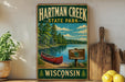 A vintage-style metal sign for Hartman Creek State Park in Wisconsin, featuring a scenic image of a lake, canoe, and surrounding forest.