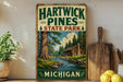 A vintage-style sign for Hartwick Pines State Park in Michigan, featuring a scenic image of a cabin surrounded by pine trees and a river.