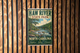 A vintage-style metal sign for Haw River State Park in North Carolina, featuring a scenic illustration of a river and forest landscape.