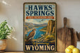 A vintage-style sign for the state recreation area of the Hawks Springs in Wyoming, featuring a scenic image of the area with a hawk perched on a rock.