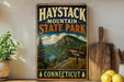 A vintage-style metal sign for Haystack Mountain State Park in Connecticut, featuring a scenic mountain landscape with a trail sign and surrounded by potted plants and kitchen utensils.