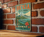 A vintage-style metal sign for He'e Eia State Park in Hawaii, featuring a tropical landscape with palm trees, mountains, and a body of water.