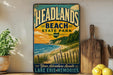 A vintage-style sign for Headlands Beach State Park in Ohio, featuring a scenic beach landscape with a sunset over the water.