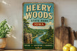 A vintage-style sign for Heery Woods State Park in Iowa, featuring a scenic image of a river and forest landscape.