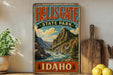 A vintage-style metal sign for Hells Gate State Park in Idaho, featuring a scenic mountain landscape with a river flowing through it.