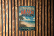 A vintage-style metal sign for Henderson Beach State Park in Florida, featuring a beach scene and palm trees, is displayed on a wooden wall.