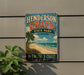 A vintage-style metal sign for Henderson Beach State Park in Florida, featuring a beach scene with palm trees and a clear blue sky.