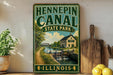 A vintage-style sign for Hennepin Canal State Park in Illinois, featuring a scenic illustration of a canal, bridge, and surrounding landscape.
