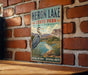 A vintage-style metal sign forHERON LAKE STATE PARK, NEW MEXICO, featuring a large heron in a grassy landscape with a lake and mountains in the background.