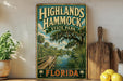 A vintage-style sign for Highlands Hammock State Park in Florida, featuring a scenic illustration of a wooden boardwalk and a body of water surrounded by palm trees.
