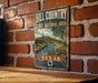 A vintage-style metal sign displaying the text "HILL COUNTRY STATE NATURAL AREA TEXAS" with a scenic landscape illustration.