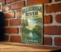 A vintage metal sign for Hillsborough River State Park in Florida, featuring a scenic illustration of a river surrounded by palm trees and a heron.