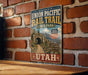 A vintage-style metal sign for the Union Pacific Rail Trail in Utah, featuring a scenic image of a tunnel and mountains.