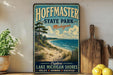 A vintage-style sign for Hoffman State Park, Michigan, featuring a scenic beach landscape with a pine tree and a wooden paddleboard.