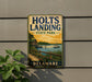 A vintage-style sign for Holts Landing State Park in Delaware, featuring a scenic image of a boat on a lake and a wooden dock.