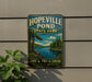 A vintage-style metal sign for Hopeville Pond State Park in Connecticut, featuring a scenic landscape with a lake, trees, and mountains.