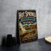 A vintage-style sign for Hot Springs State Park in Wyoming, featuring a scenic landscape with a hot spring and mountains in the background.