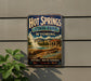A vintage-style sign for Hot Springs State Park in Wyoming, featuring a scenic image of the park's natural hot springs and surrounding landscape.