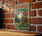 A vintage-style metal sign for Humbold Redwoods State Park in California, featuring a scenic illustration of the park's iconic redwood trees.