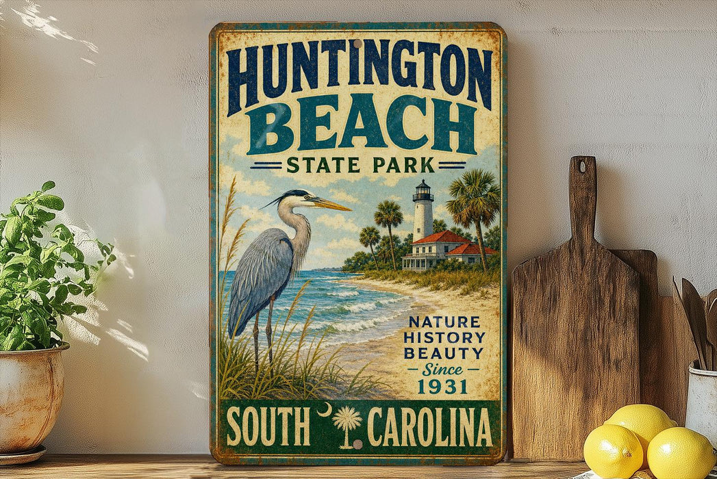 A vintage-style metal sign for Huntington Beach State Park, featuring a blue heron and a lighthouse, is displayed on a shelf next to a wooden cutting board and some lemons.