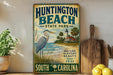 A vintage-style metal sign for Huntington Beach State Park, featuring a blue heron and a lighthouse, is displayed on a shelf next to a wooden cutting board and some lemons.